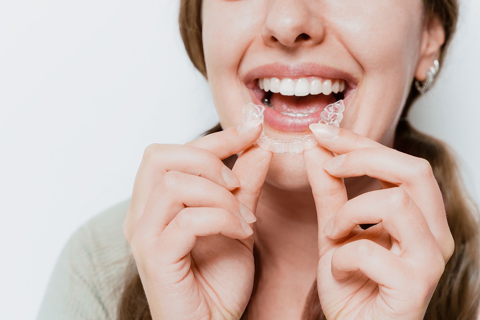 A woman is holding a clear aligner in her mouth.