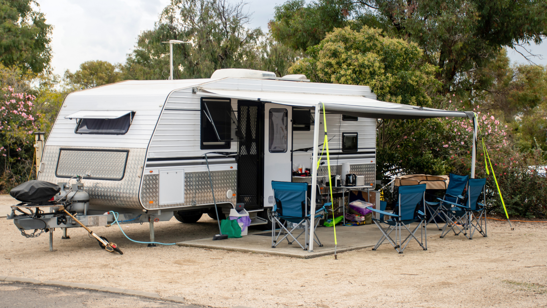 White camper trailer with awning extended, outdoor seating, and camping accessories.