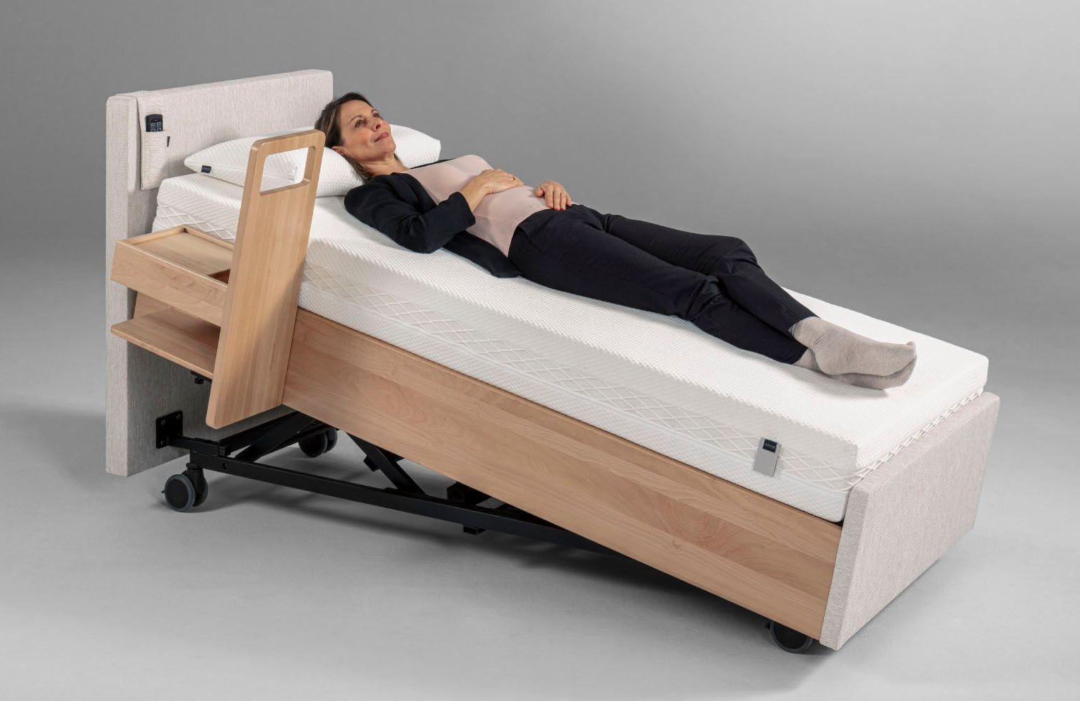 Frau ruht auf einem verstellbaren Krankenhausbett. Das Bett ist schräg gestellt und verfügt über einen Nachttisch.