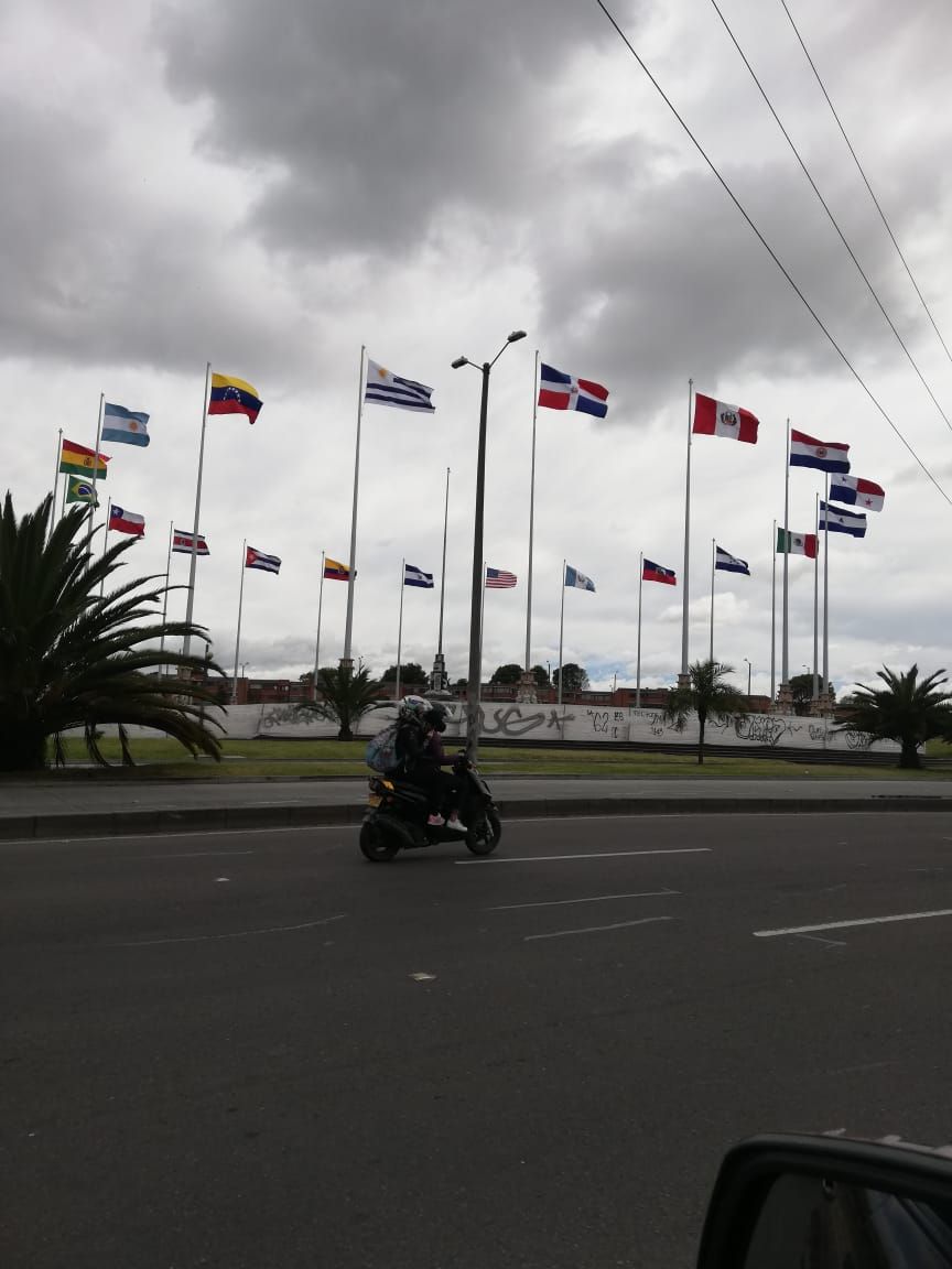 Un hombre conduce una scooter por una calle con muchas banderas ondeando al fondo.