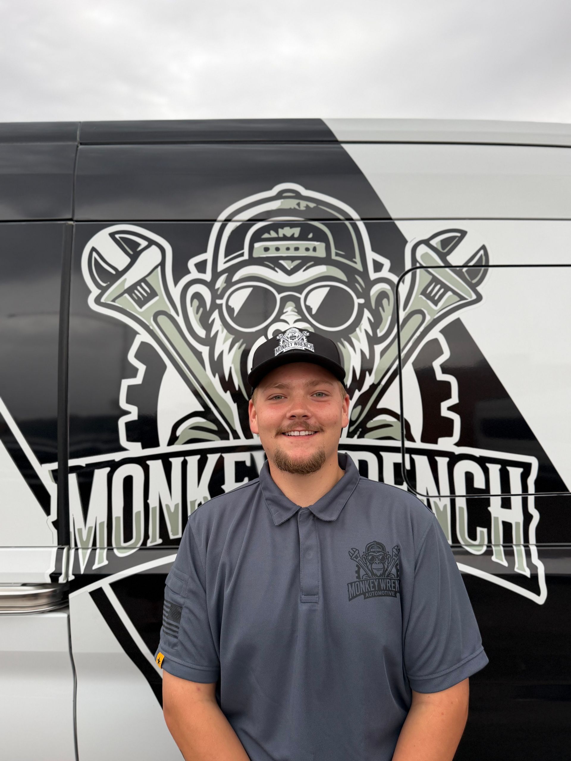 Man in sunglasses and a cap standing before a motorcycle-themed mural with crossed wrenches