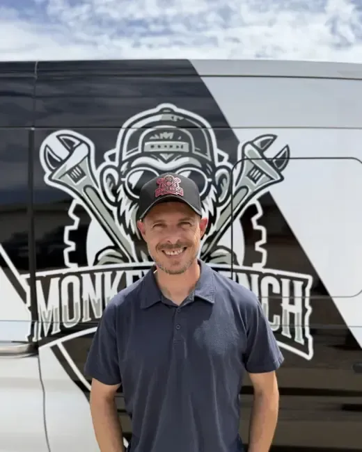Smiling man in a navy polo and cap standing in front of a branded van with a monkey wrench logo