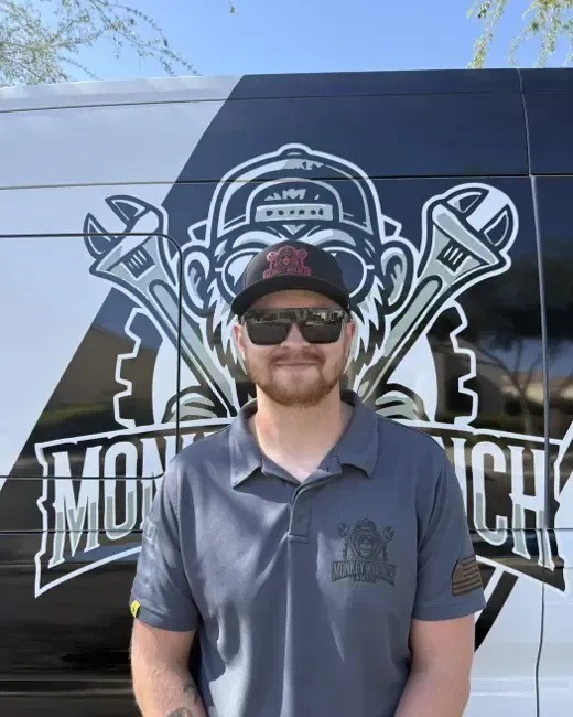 Man in sunglasses and a cap standing before a motorcycle-themed mural with crossed wrenches
