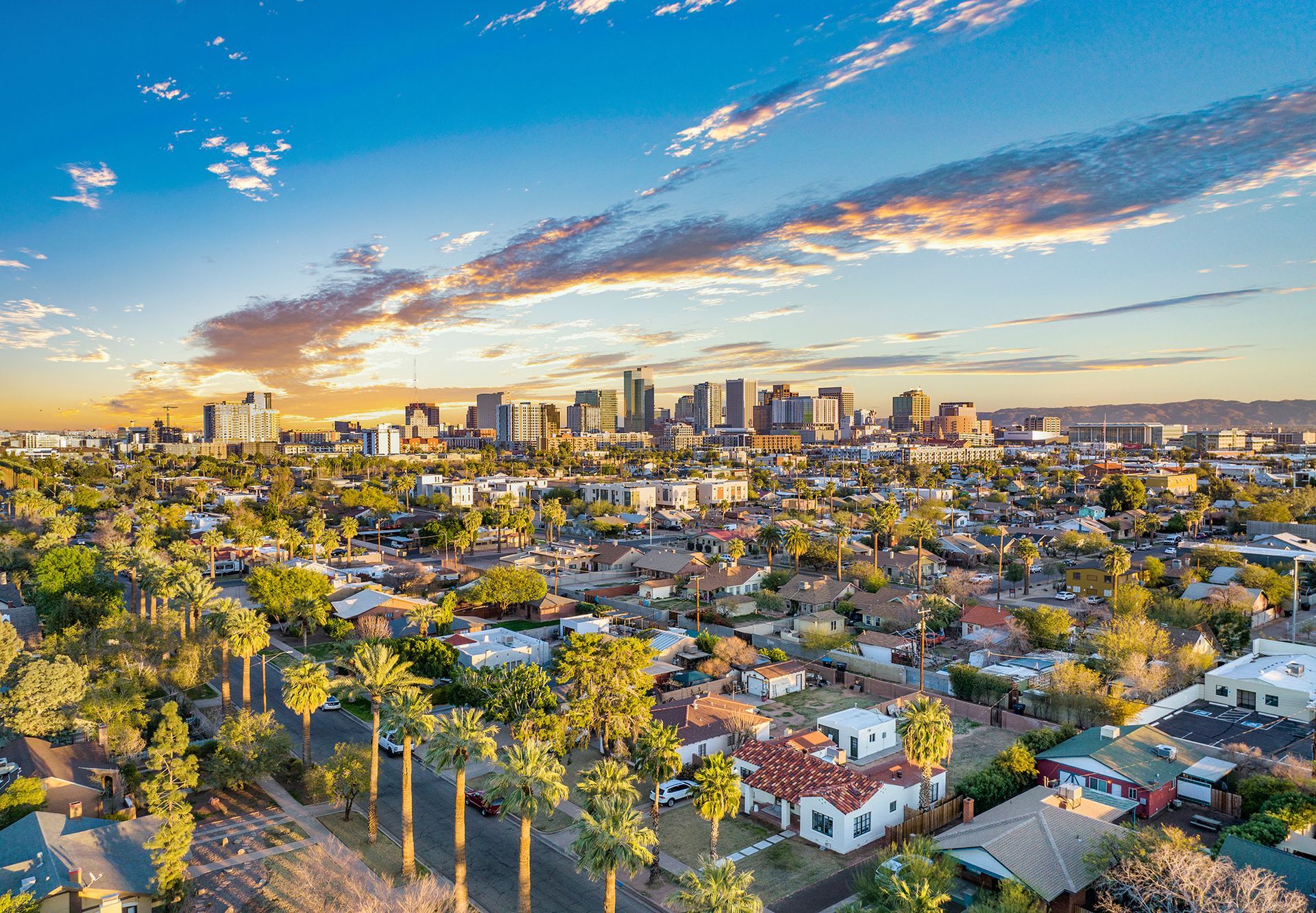 Sunset aerial view of a city skyline above a neighborhood with palm trees and colorful houses