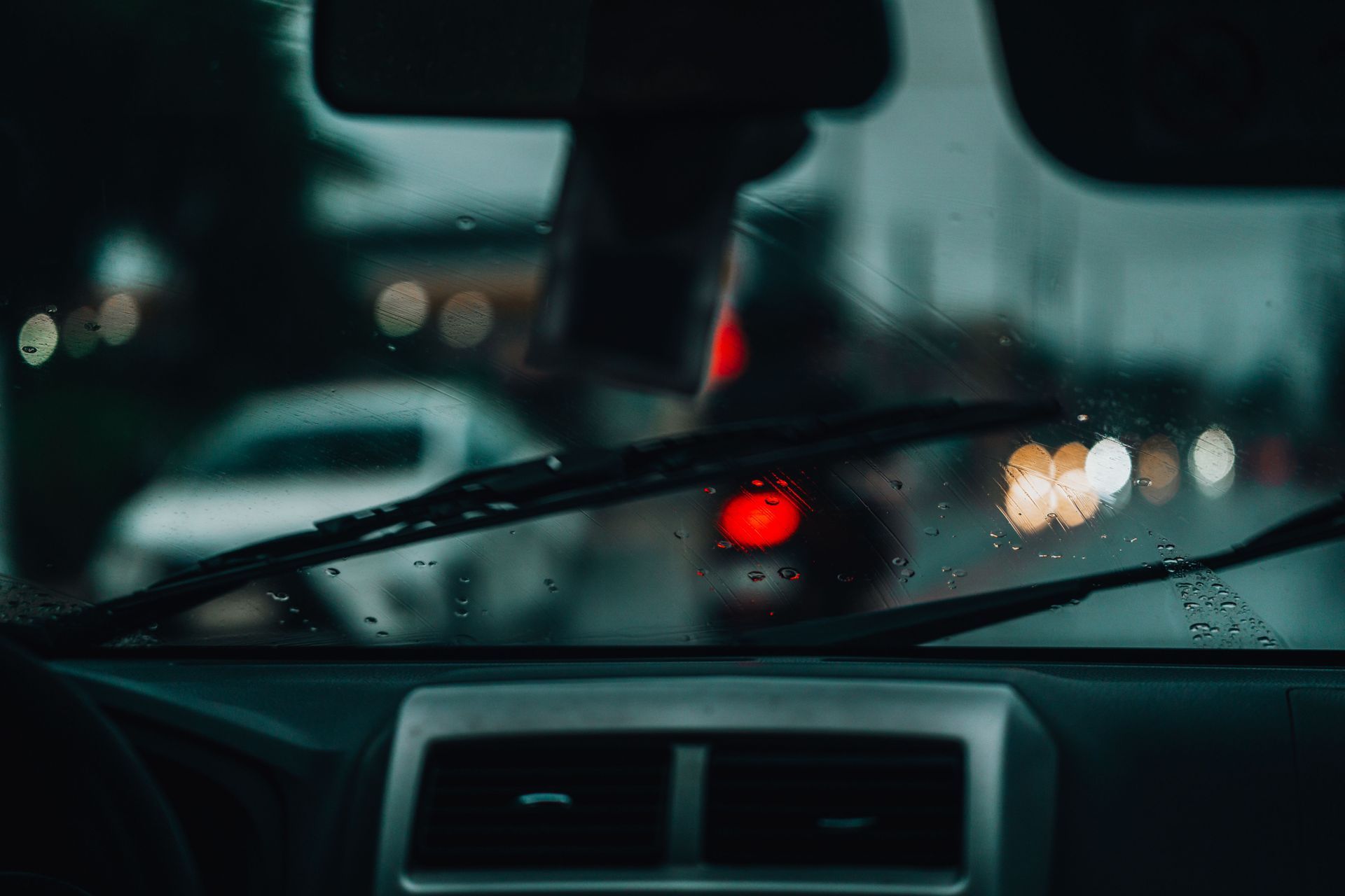 Rainy car interior looking through a wet windshield at blurred red brake lights in traffic