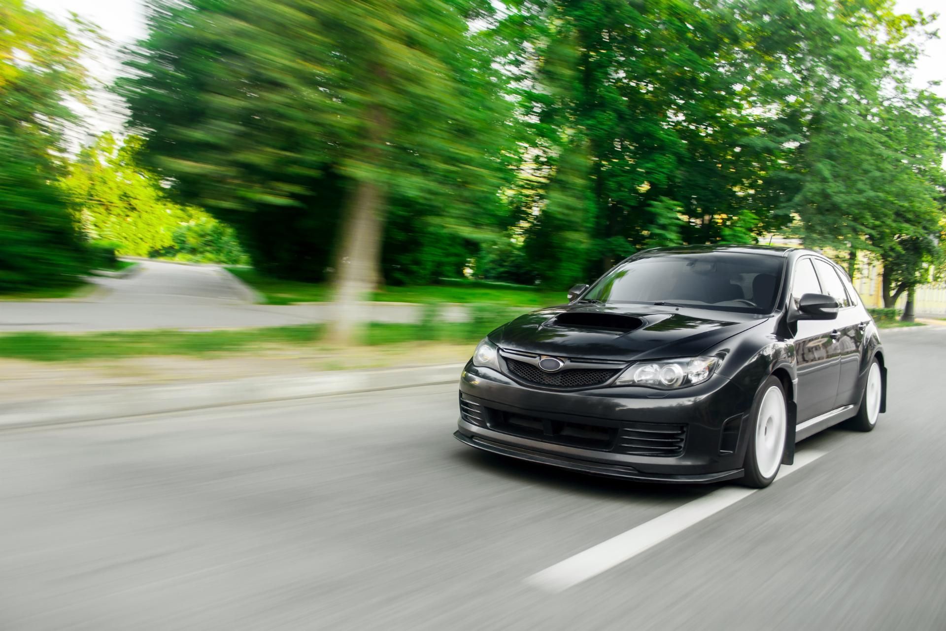 Black car driving on a tree-lined road, motion blurred background