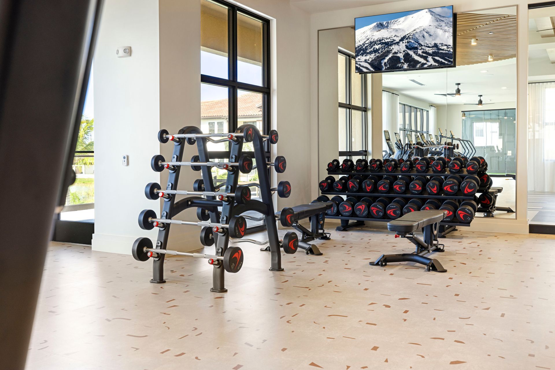 A gym with a lot of dumbbells and a tv on the wall at Corsa at Estero Crossing.