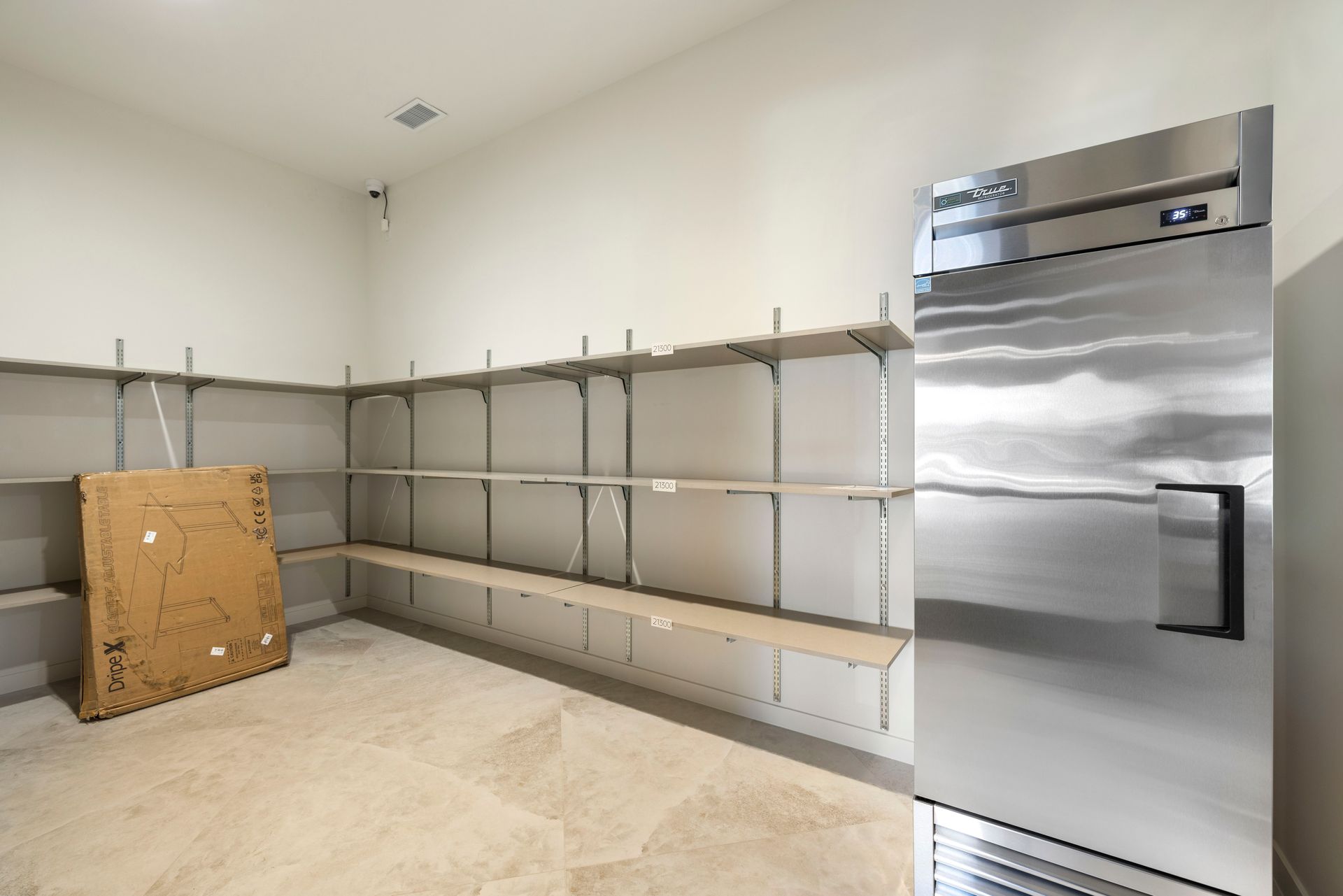 An empty room with stainless steel shelves and a stainless steel refrigerator at Corsa at Estero Crossing.