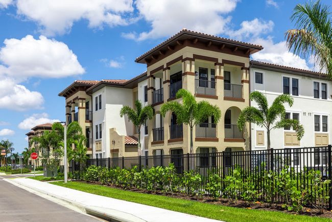 A large apartment building with a fence and palm trees in front of it at Corsa at Estero Crossing.