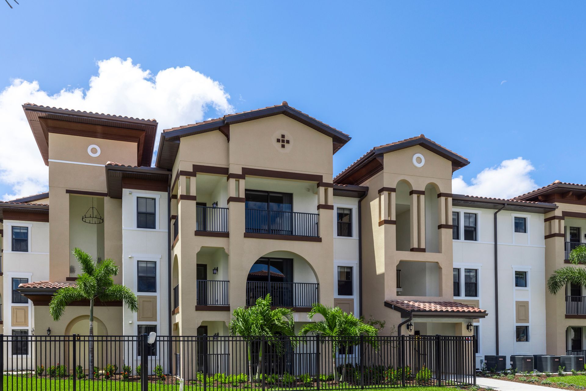 A large apartment building with a fence around it and a blue sky in the background at Corsa at Estero Crossing.