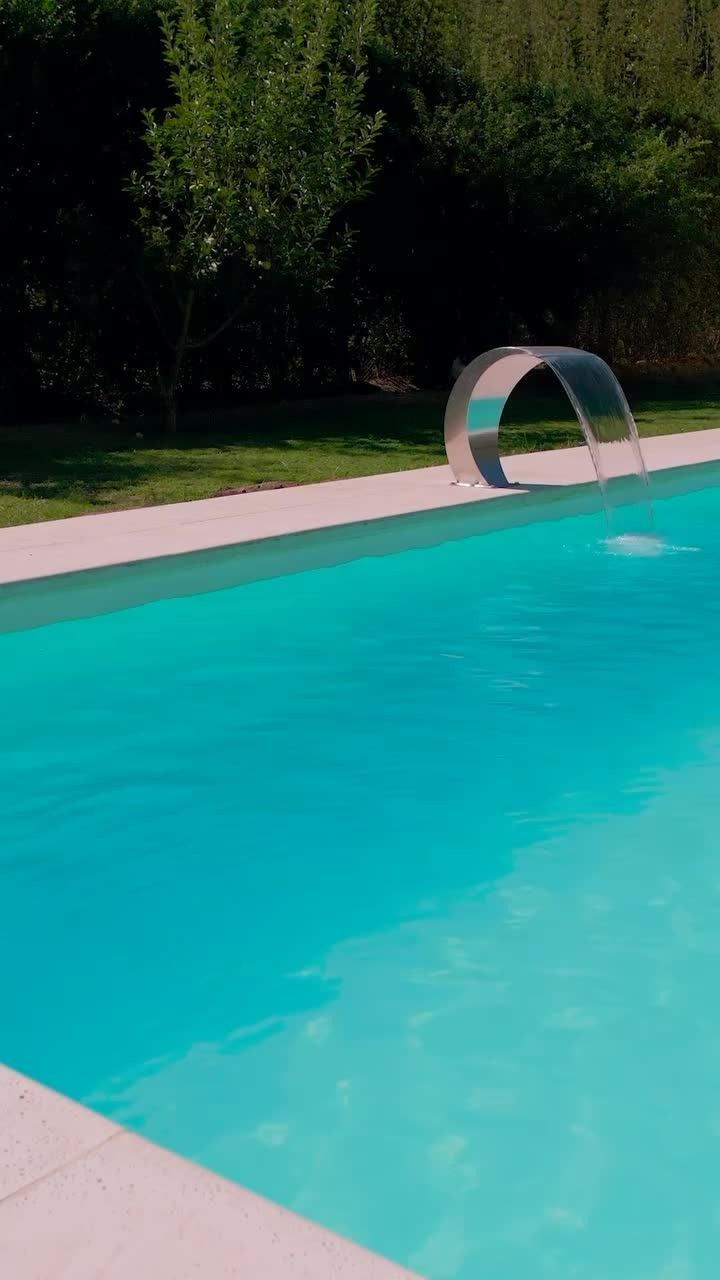 Piscina de color turquesa junto a una terraza de azulejos y un aro de metal cerca del borde más alejado