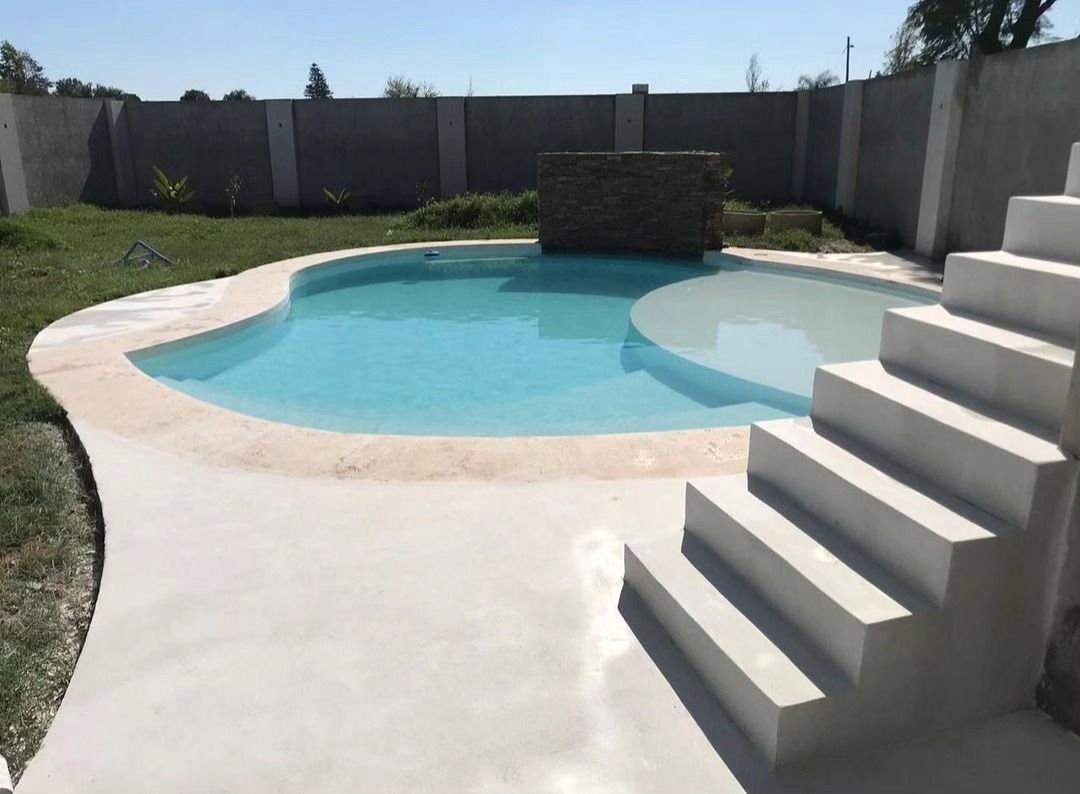 Piscina en el patio trasero con agua azul claro, terraza de hormigón y escalones en primer plano.