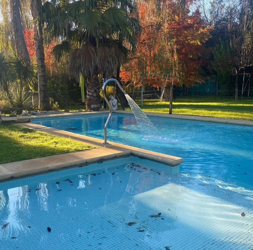 Piscina al aire libre con tobogán acuático, agua azul y árboles bajo la luz del sol otoñal.