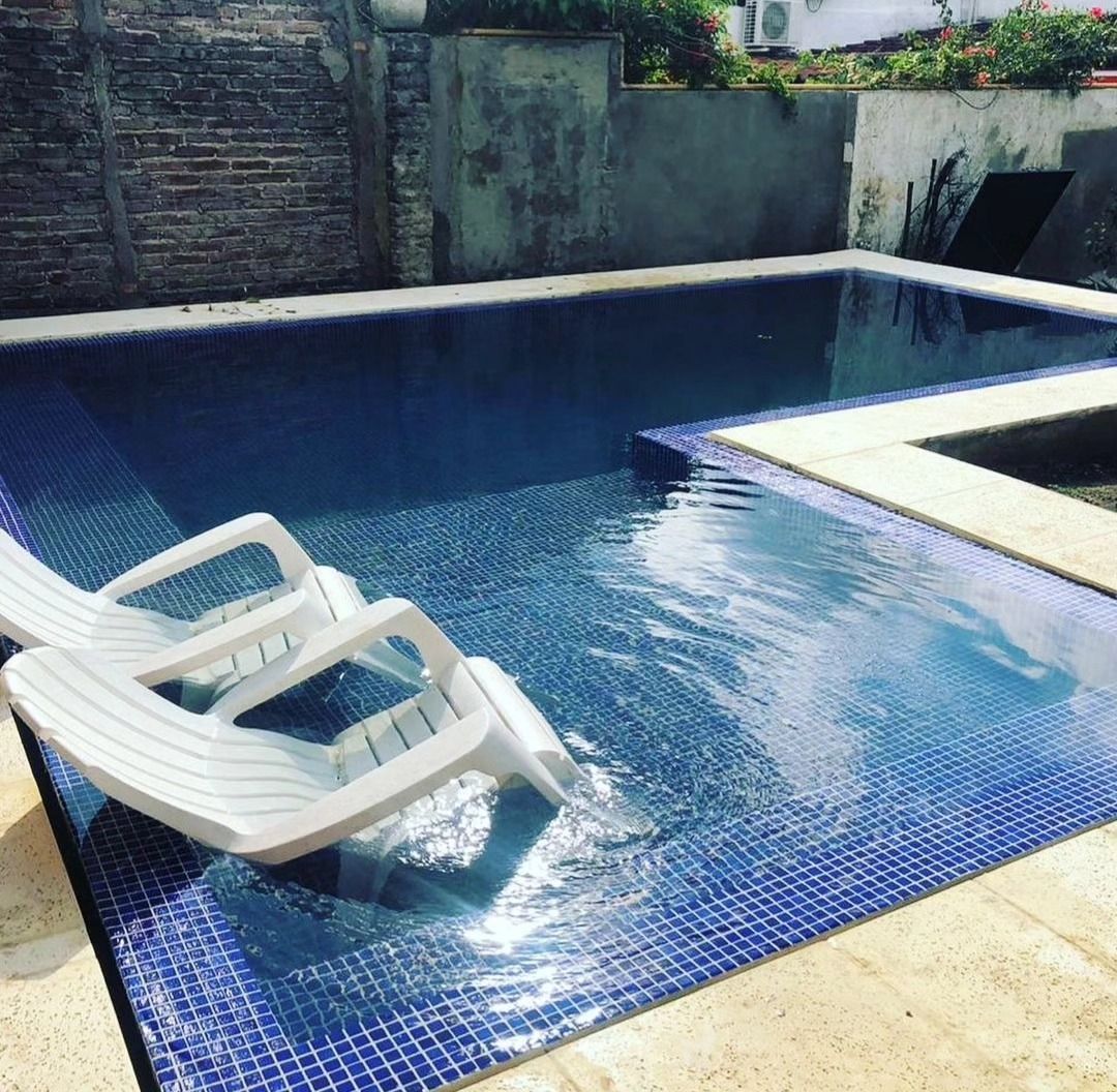 Pequeña piscina en el patio trasero con agua azul y dos tumbonas blancas en el borde.
