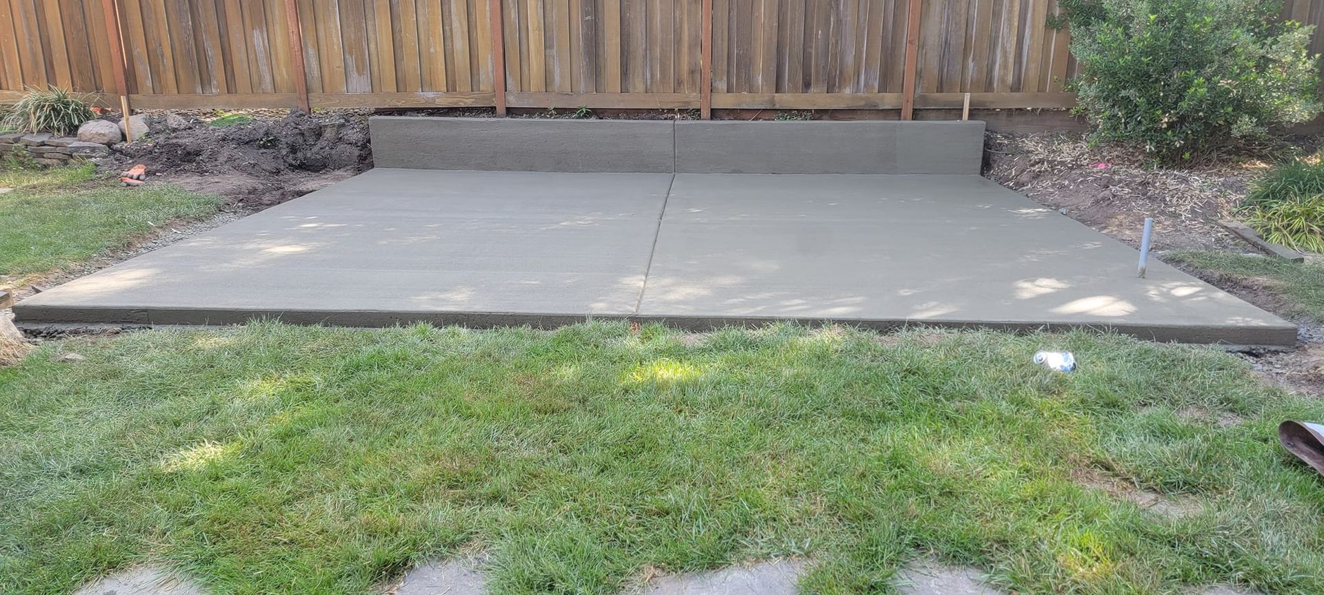 A concrete patio is being built in a backyard next to a wooden fence.