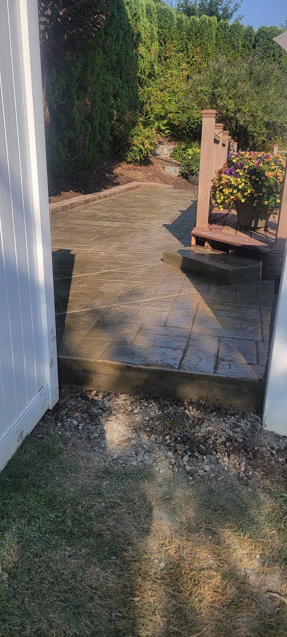 A concrete walkway leading to a deck next to a white fence.