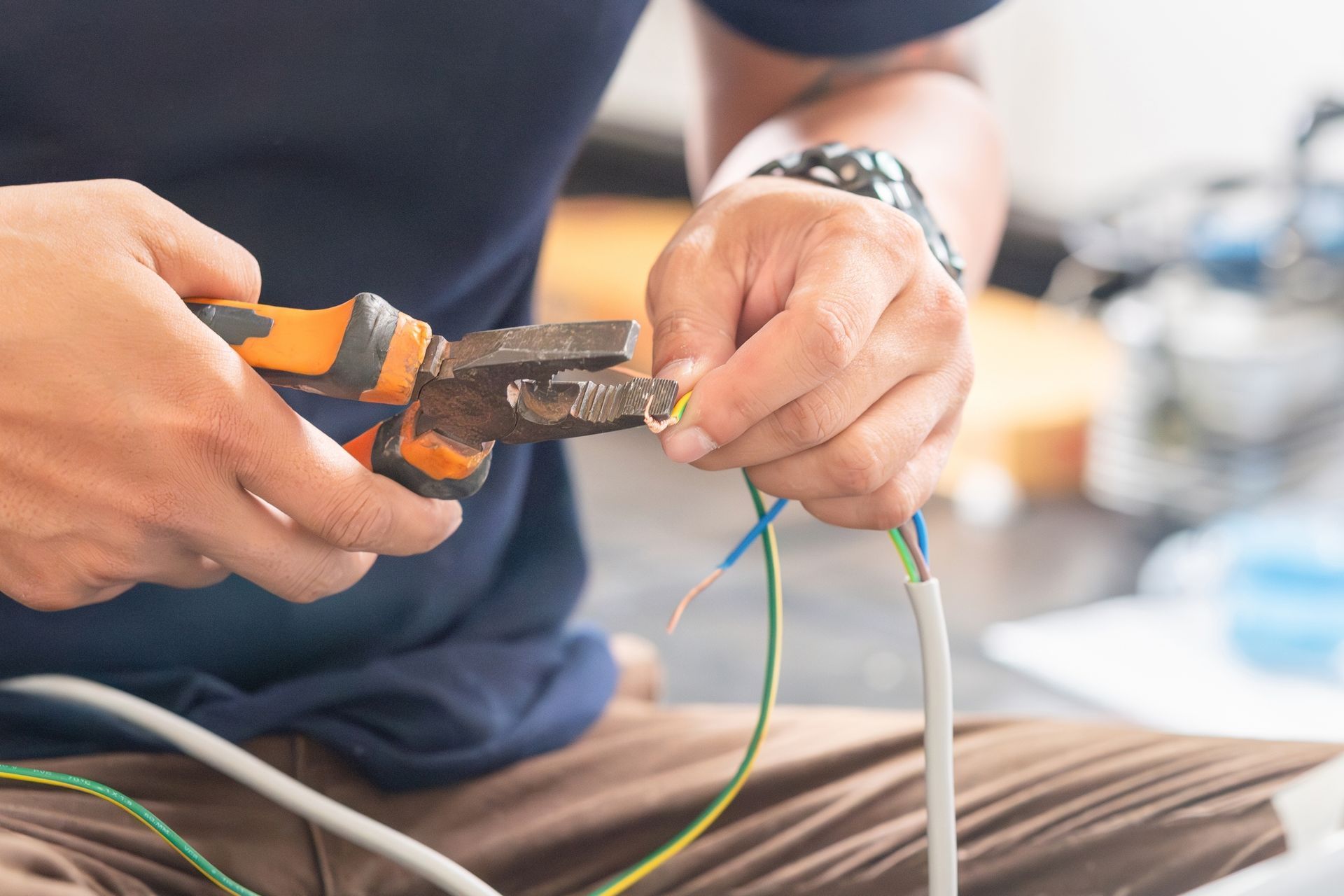 A person using pliers to strip wires. Indoors, cutting a multi-colored electrical cable.
