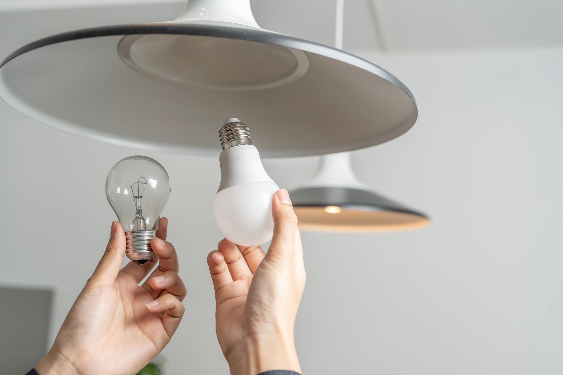 Hands holding a light bulb and LED bulb, near a ceiling lamp.