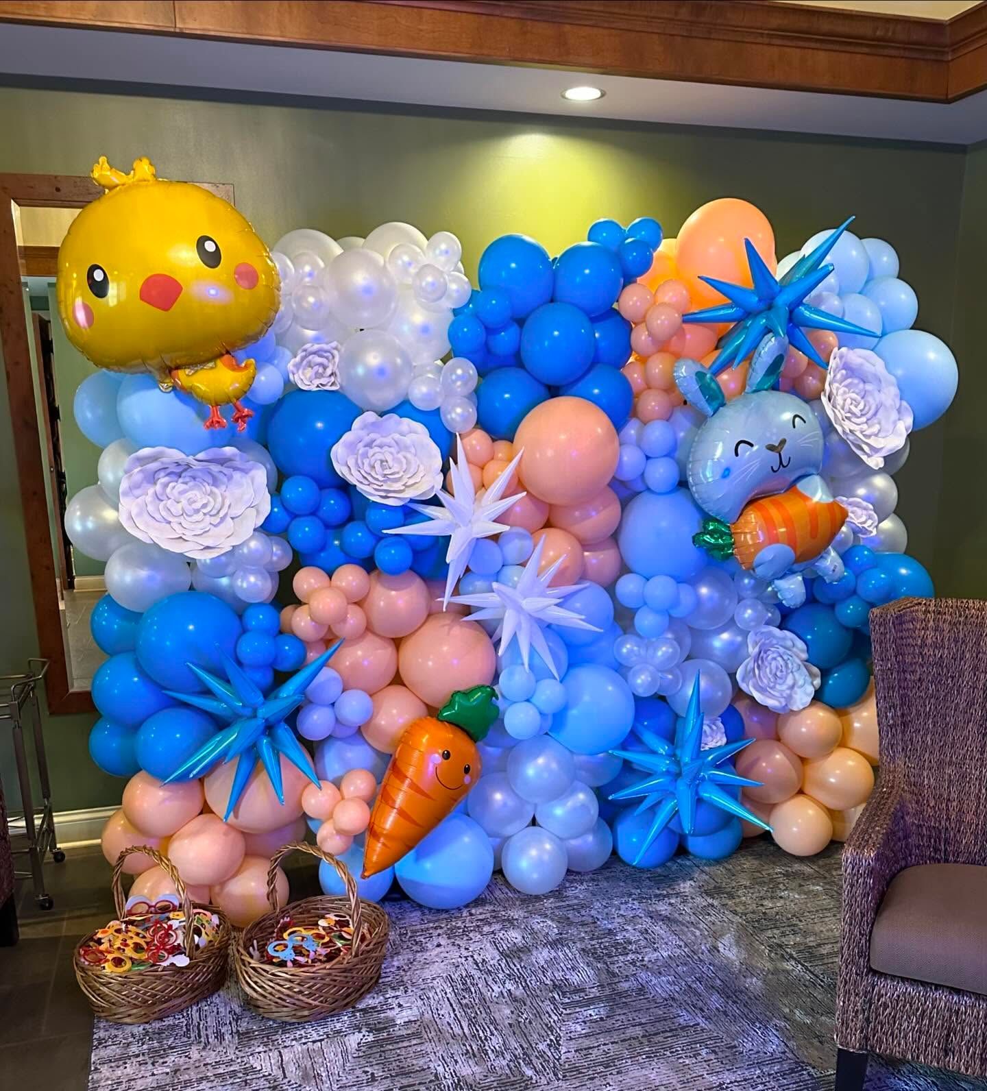 Blue and peach balloon wall with cartoon fruit balloons and flowers in a decorated indoor party setting