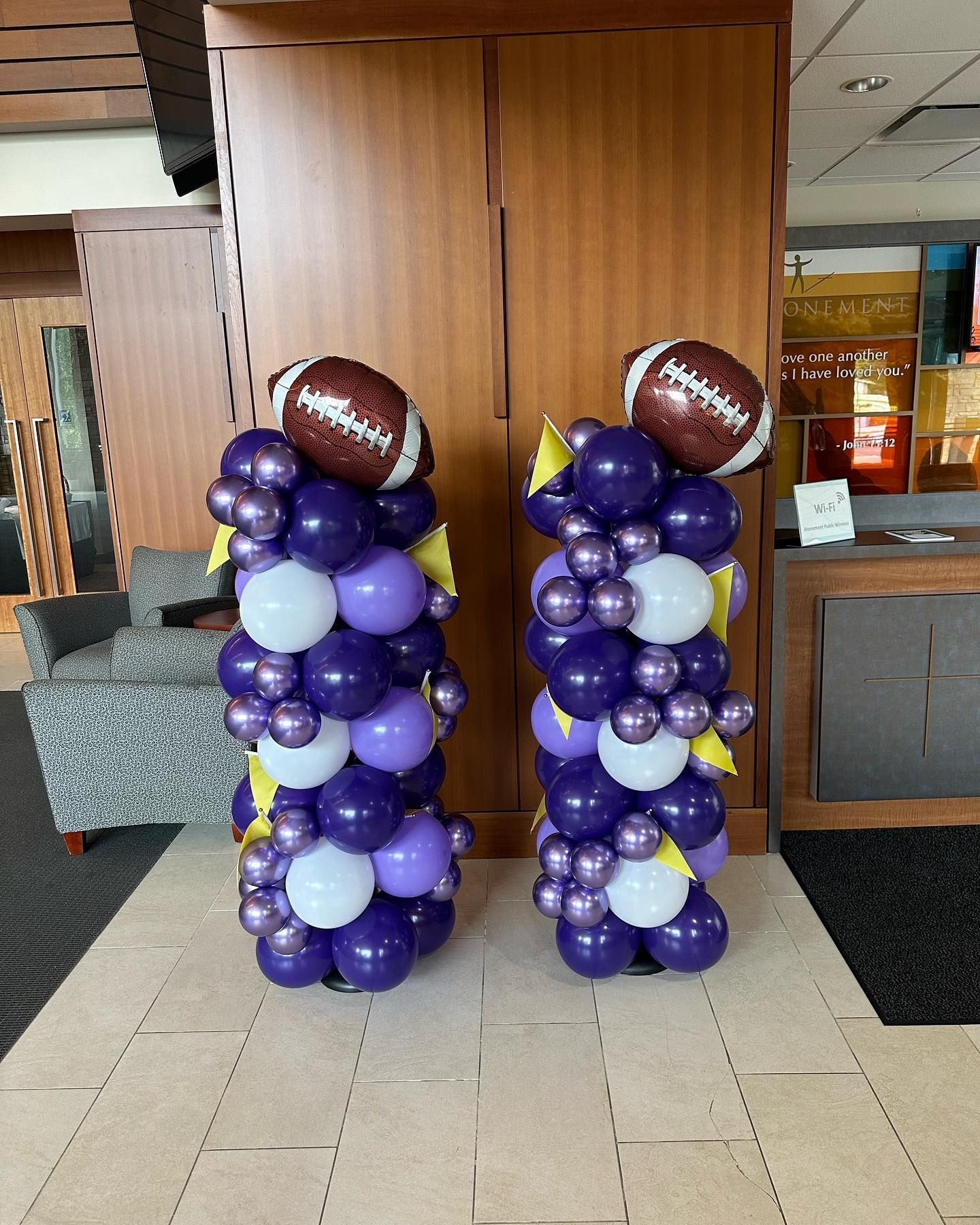 Two columns made of purple and white balloons with footballs on top.