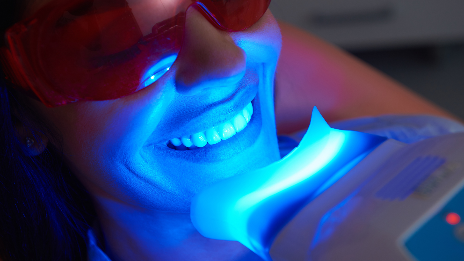 Woman undergoing teeth whitening treatment with blue light.
