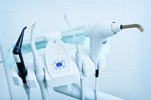 Dental tools mounted on a white bracket, including a black suction tube, a light, and controls.