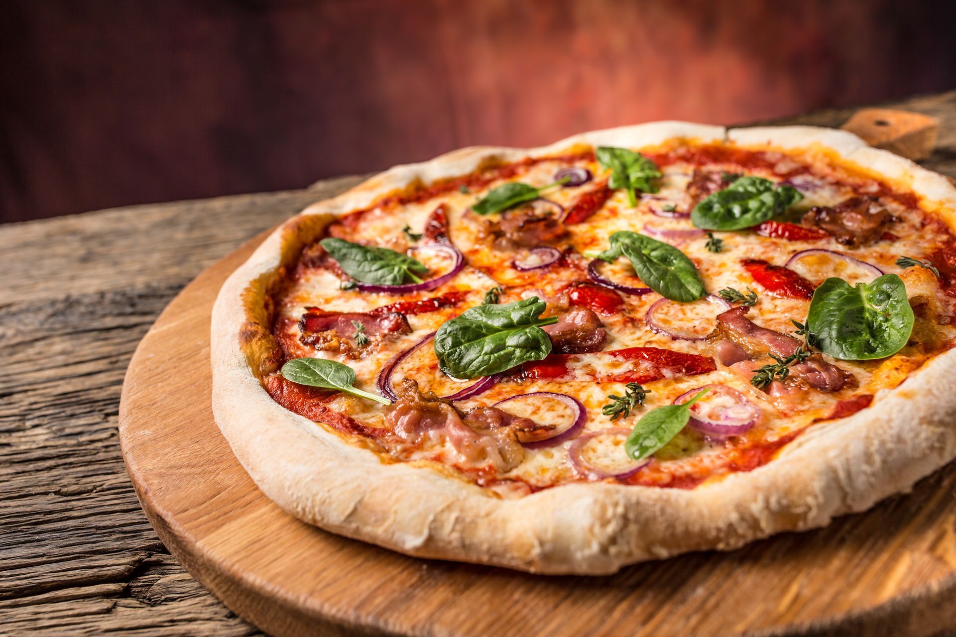 A freshly baked pizza topped with spinach, red onions, peppers, and melted cheese A freshly baked pizza topped with spinach, red onions, peppers, and melted cheese