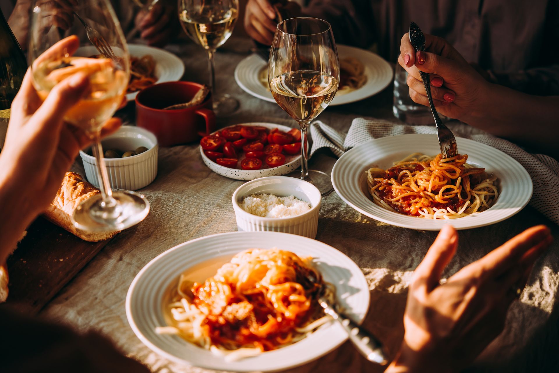 Friends sharing pasta and wine at a warmly lit dinner table