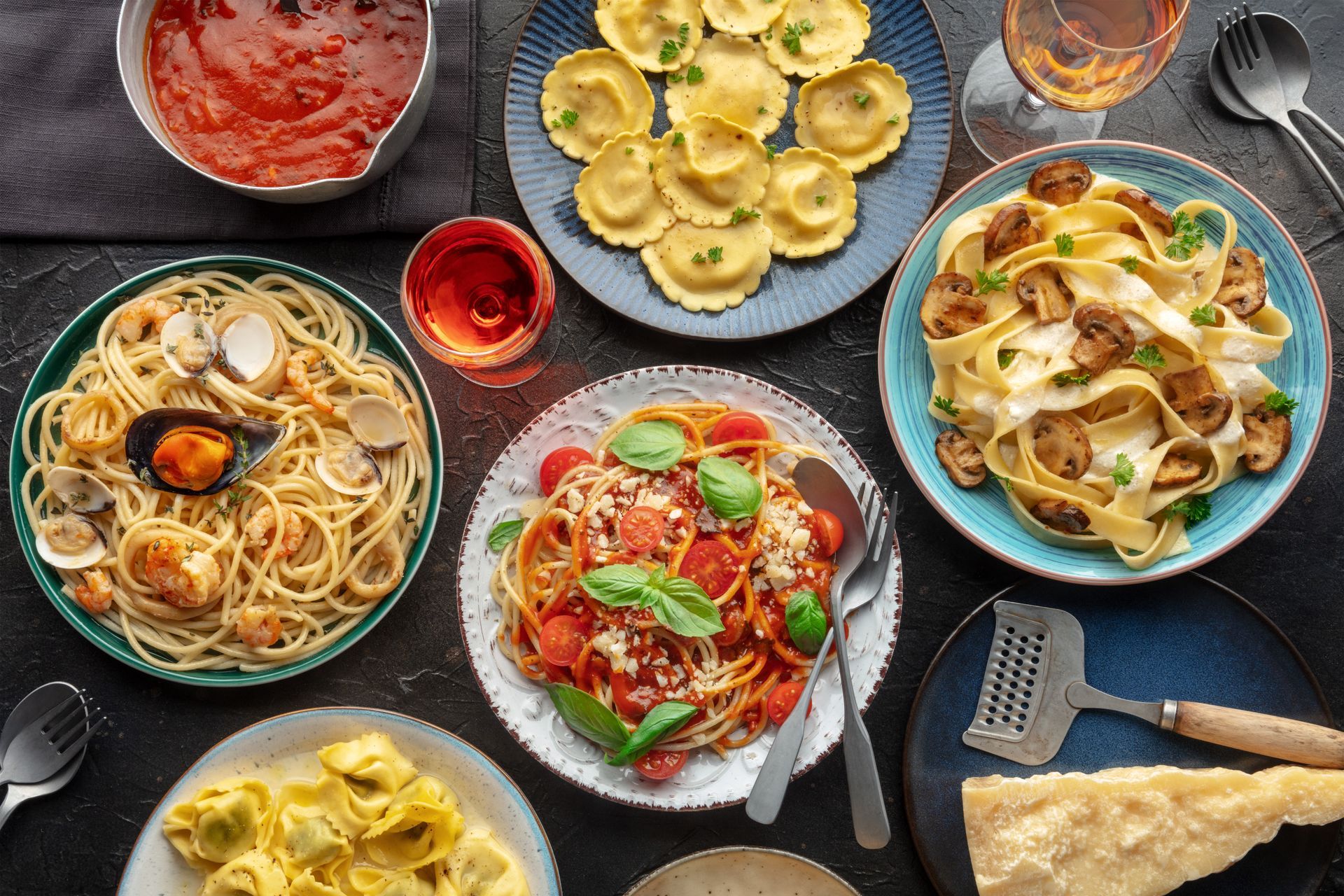 Assorted pasta dishes on plates with sauces and utensils arranged on a dark table.