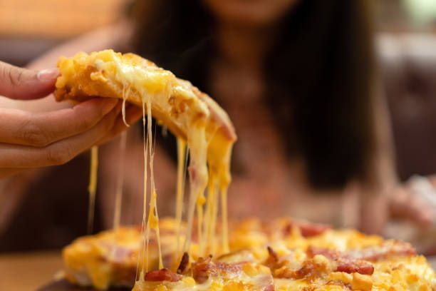 Hand pulling a cheesy slice from a hot bacon pizza, showing gooey melt for pizza delivery. 