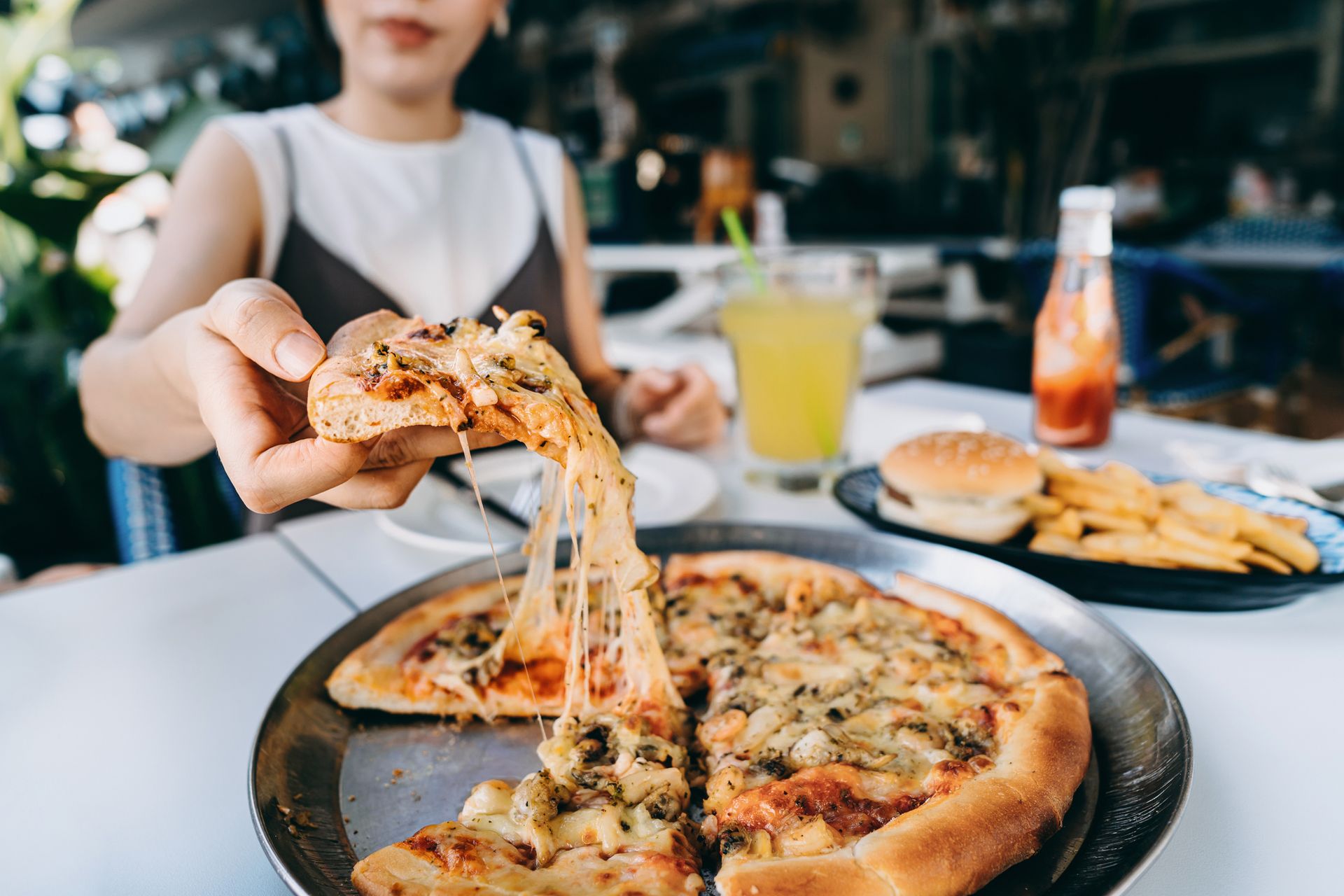 Close up of young Asian woman getting a slice of freshly made cheesy seafood pizza.