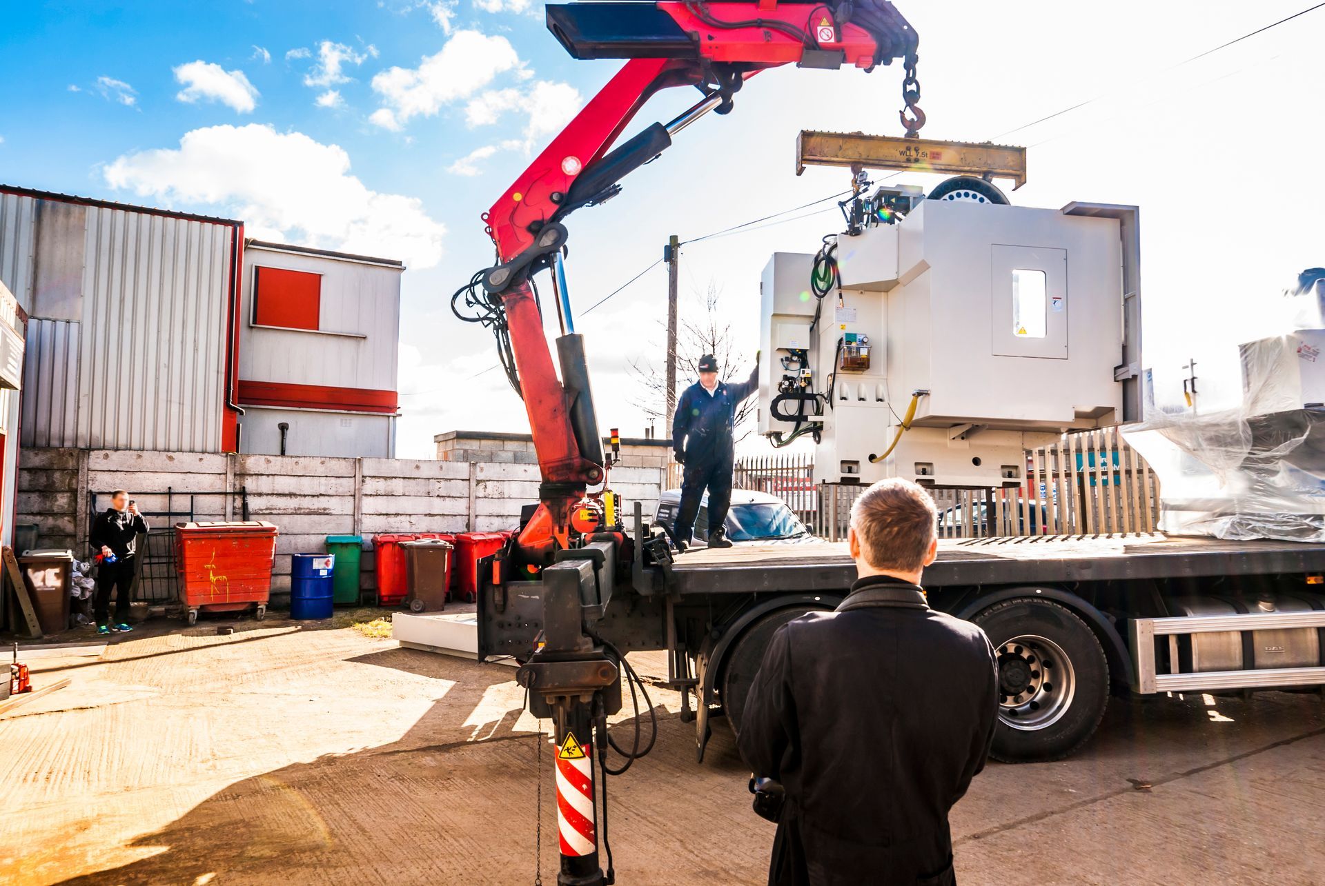 A crane operator is using a truck for lifting a heavy CNC machine while a worker looks on. A crane operator is using a truck for lifting a heavy CNC machine while a worker looks on.