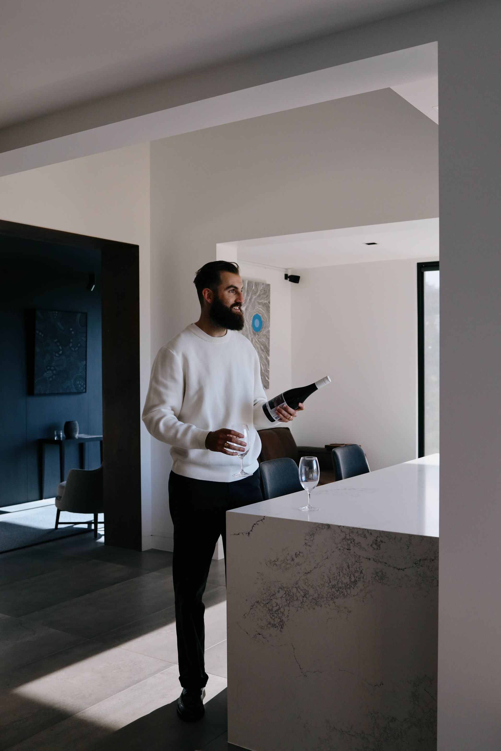 A man is standing in a kitchen holding a bottle of wine.