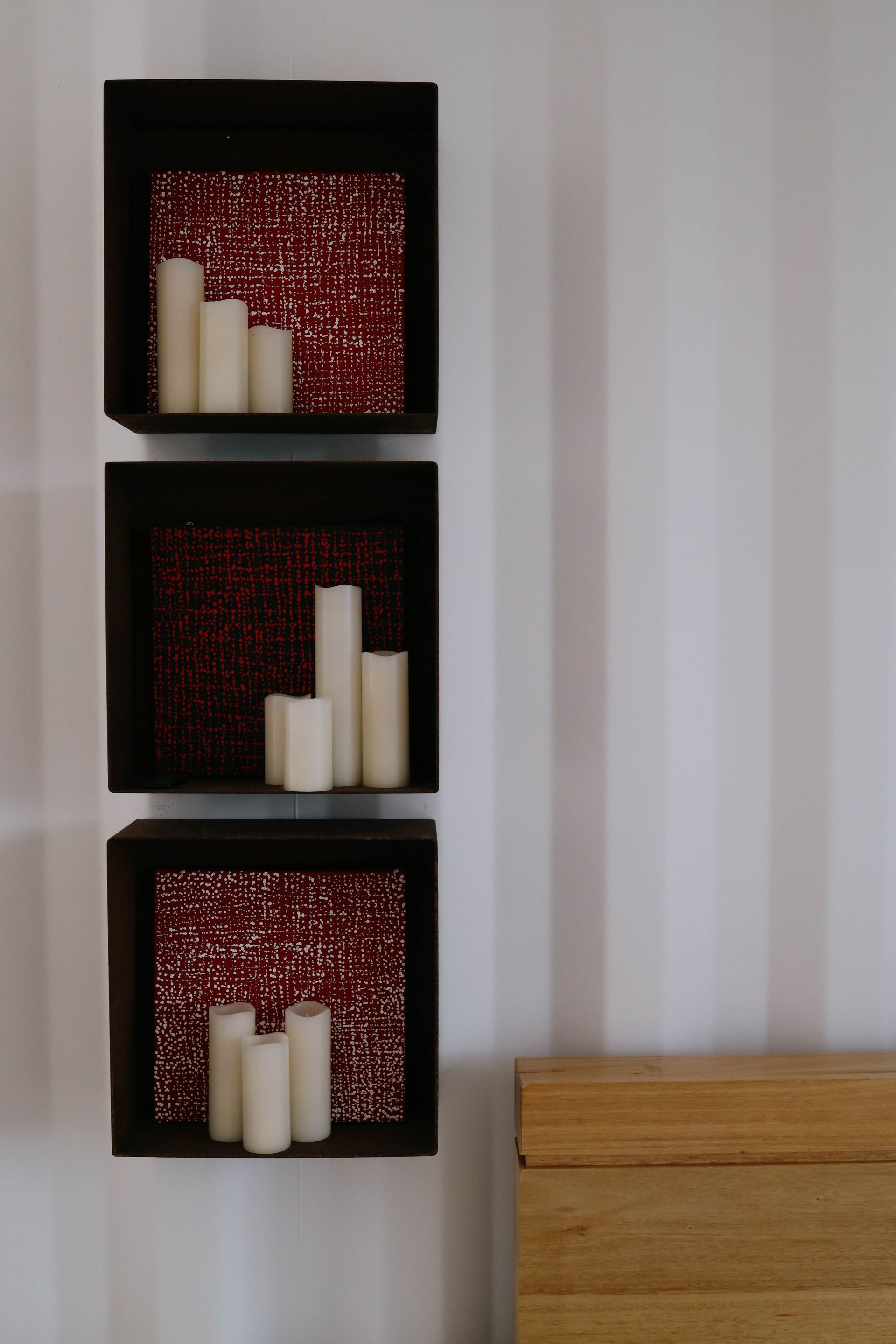 Three shelves with candles in them on a wall