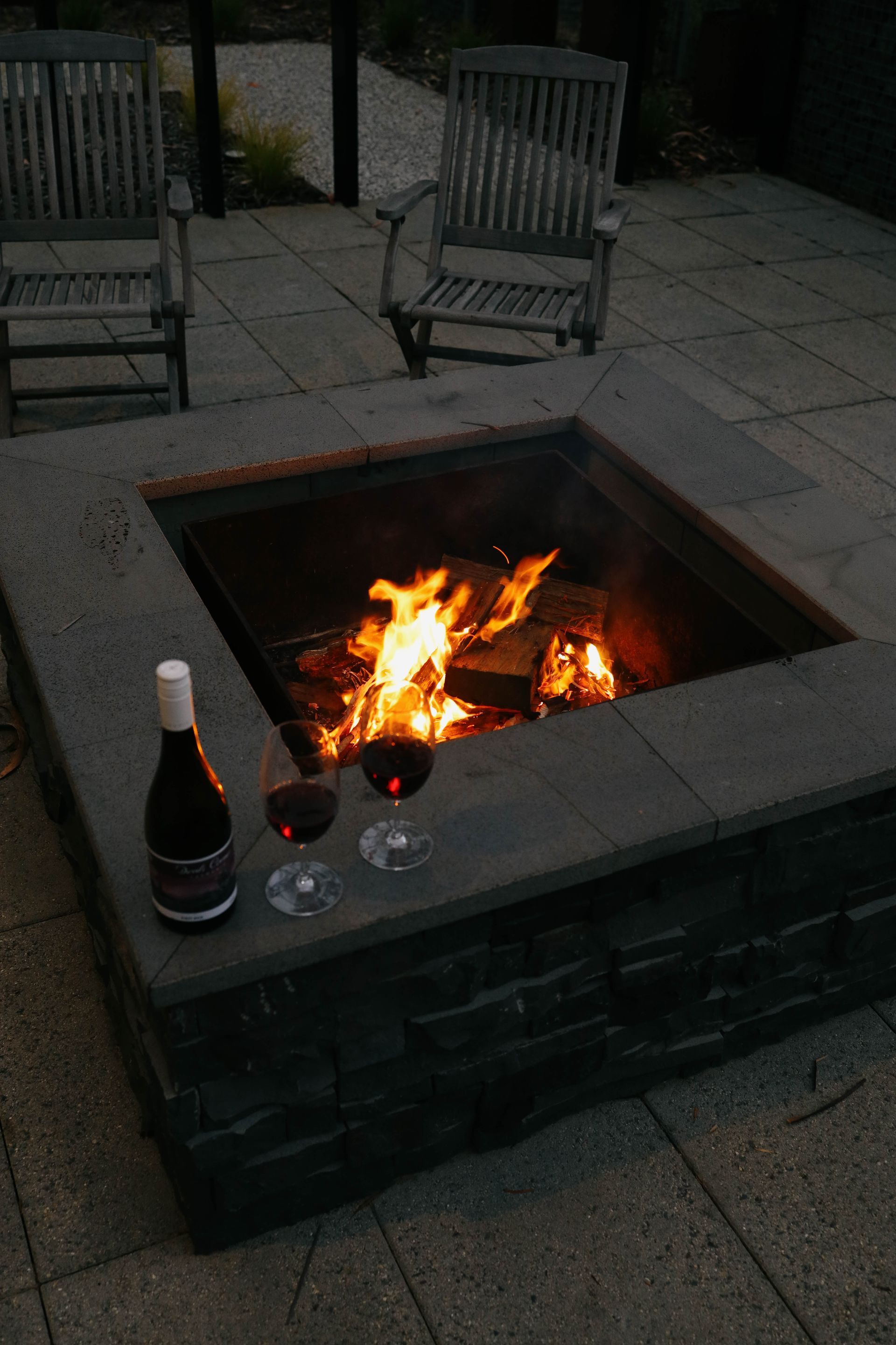 A fire pit with two glasses of wine and a bottle of wine.