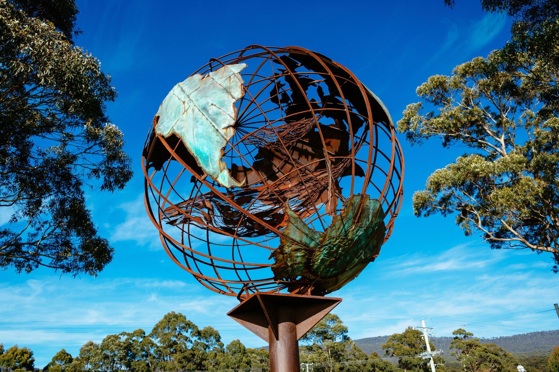 A statue of a globe on a pole with trees in the background