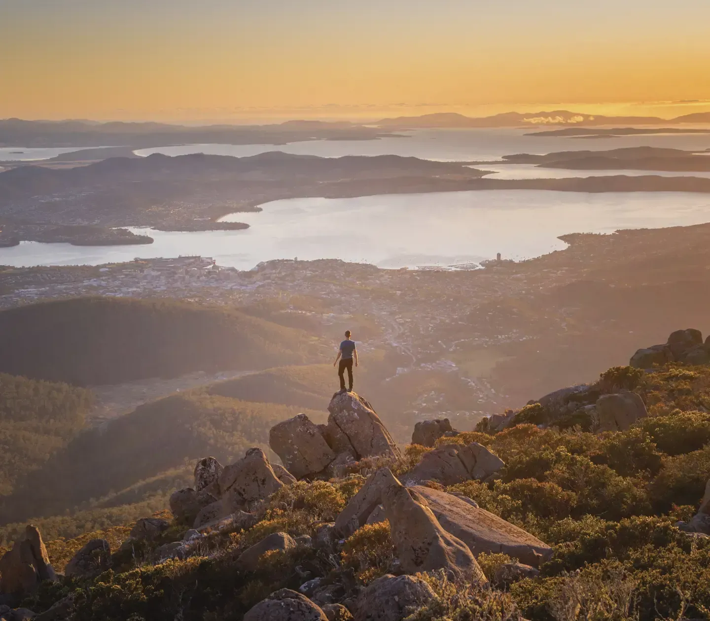 A man is standing on top of a rock overlooking a lake.