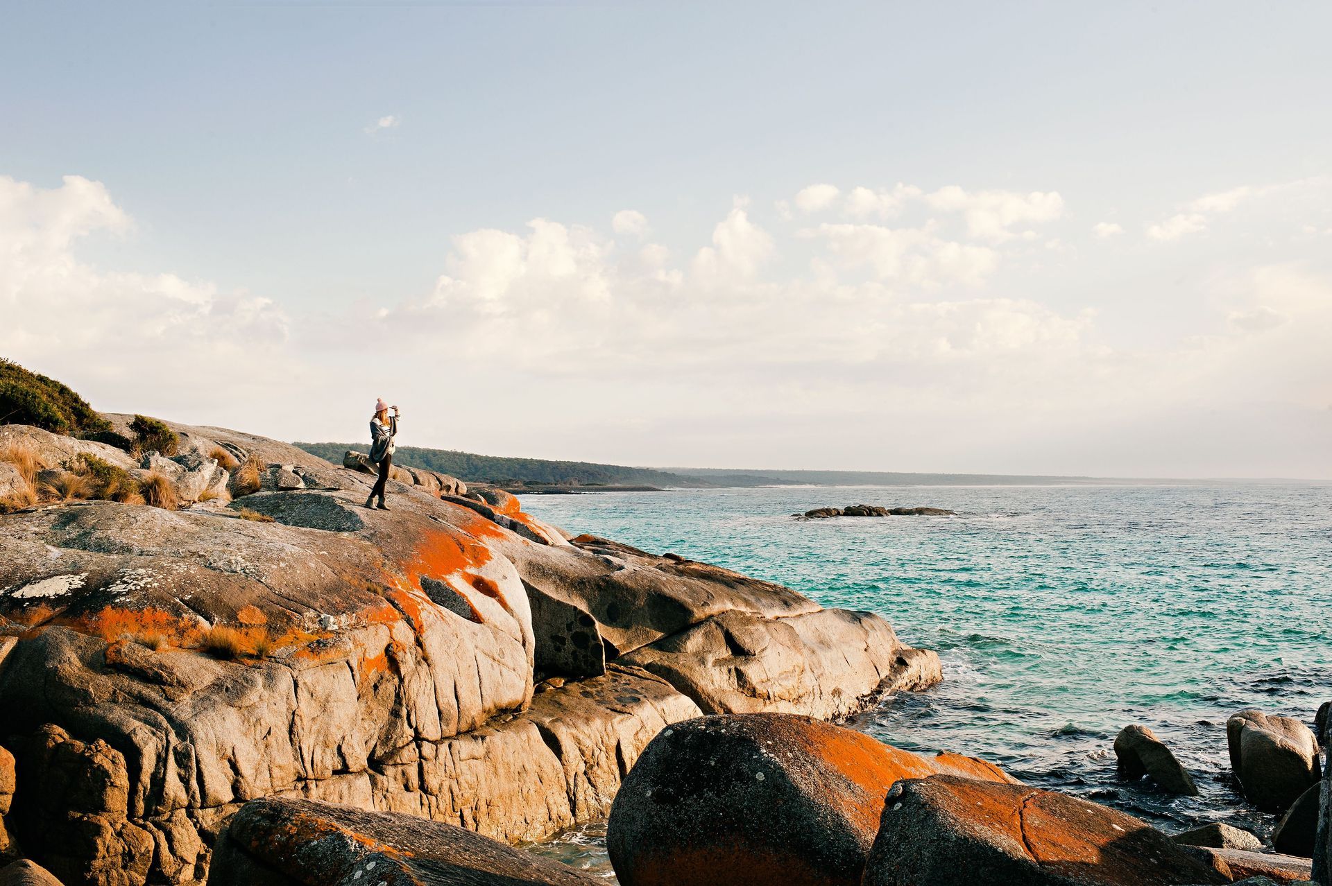 A person is standing on a rocky cliff overlooking the ocean.