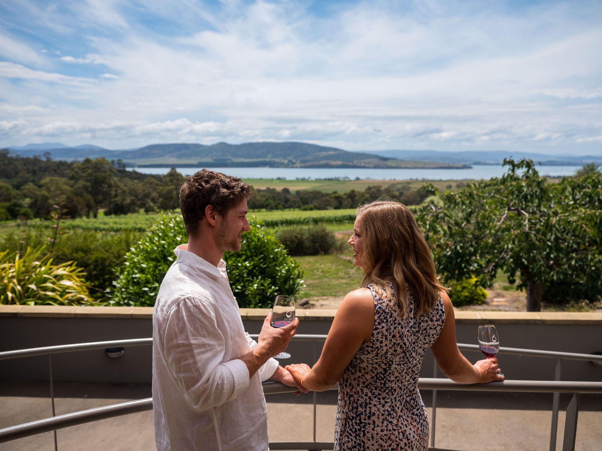 A man and a woman are standing on a balcony holding wine glasses.
