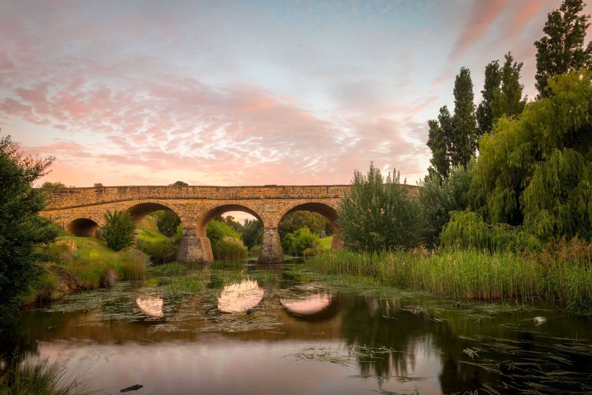 A stone bridge over a river with a sunset in the background.