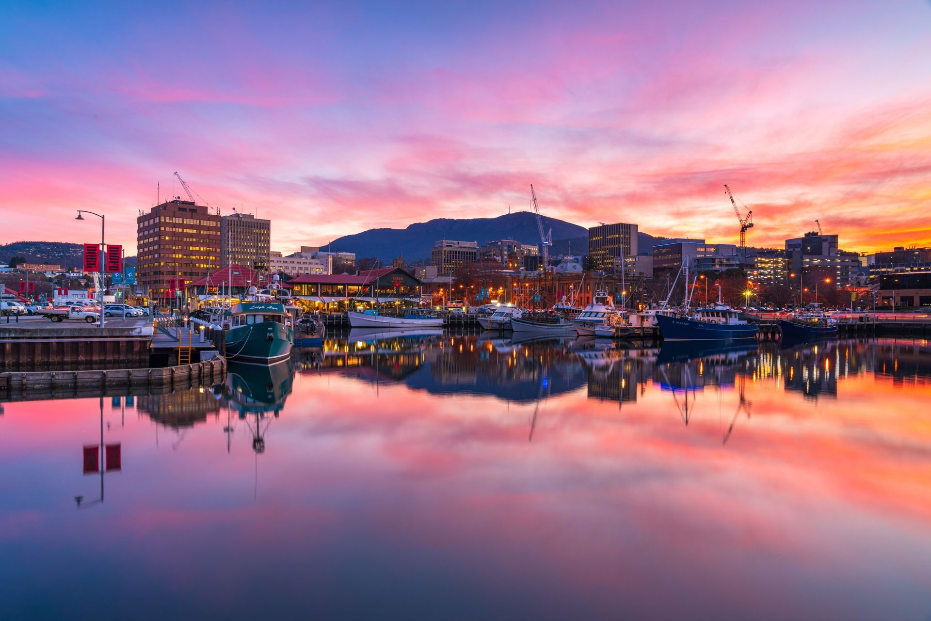 A sunset over a harbor with boats docked and a city in the background.