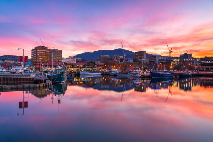 A sunset over a harbor with boats docked and a city in the background.