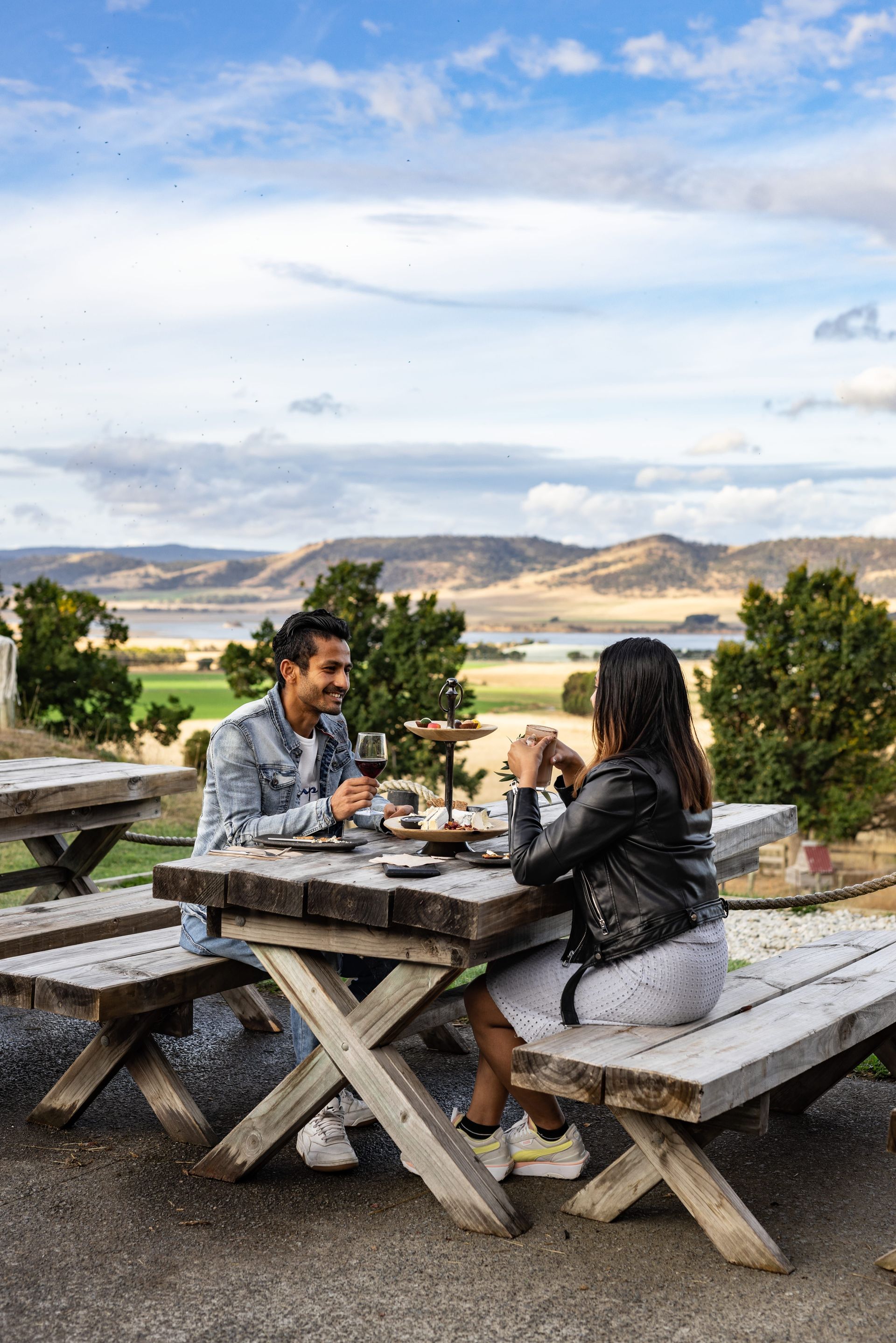 A man and a woman are sitting at a picnic table drinking wine.