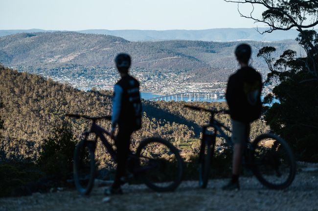 Two people are standing next to their bicycles on top of a hill looking out over a city.
