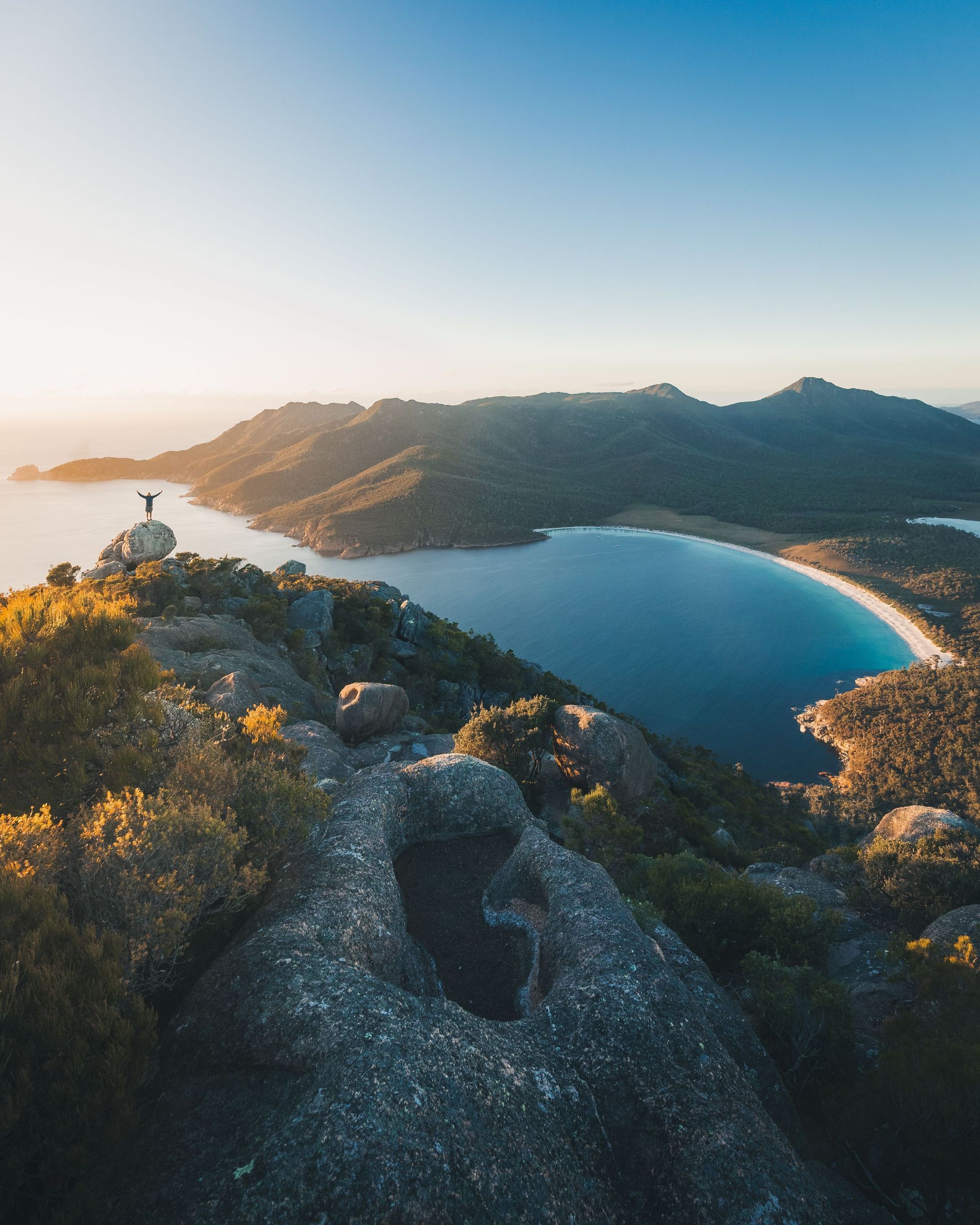 A person is standing on top of a mountain overlooking a body of water.