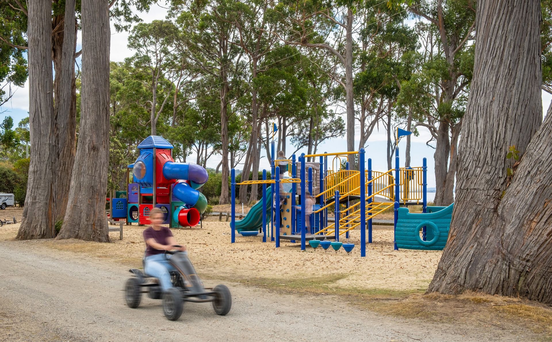 A young boy is riding a go kart in front of a playground.
