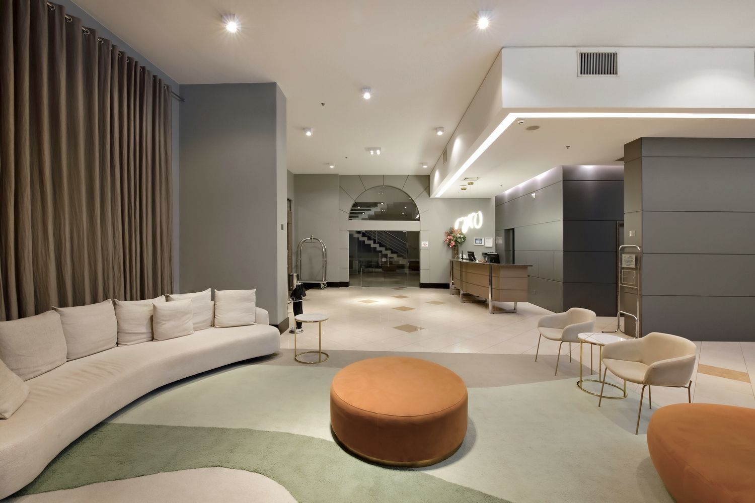 Um lobby com um sofá, cadeiras, pufe e mesas.