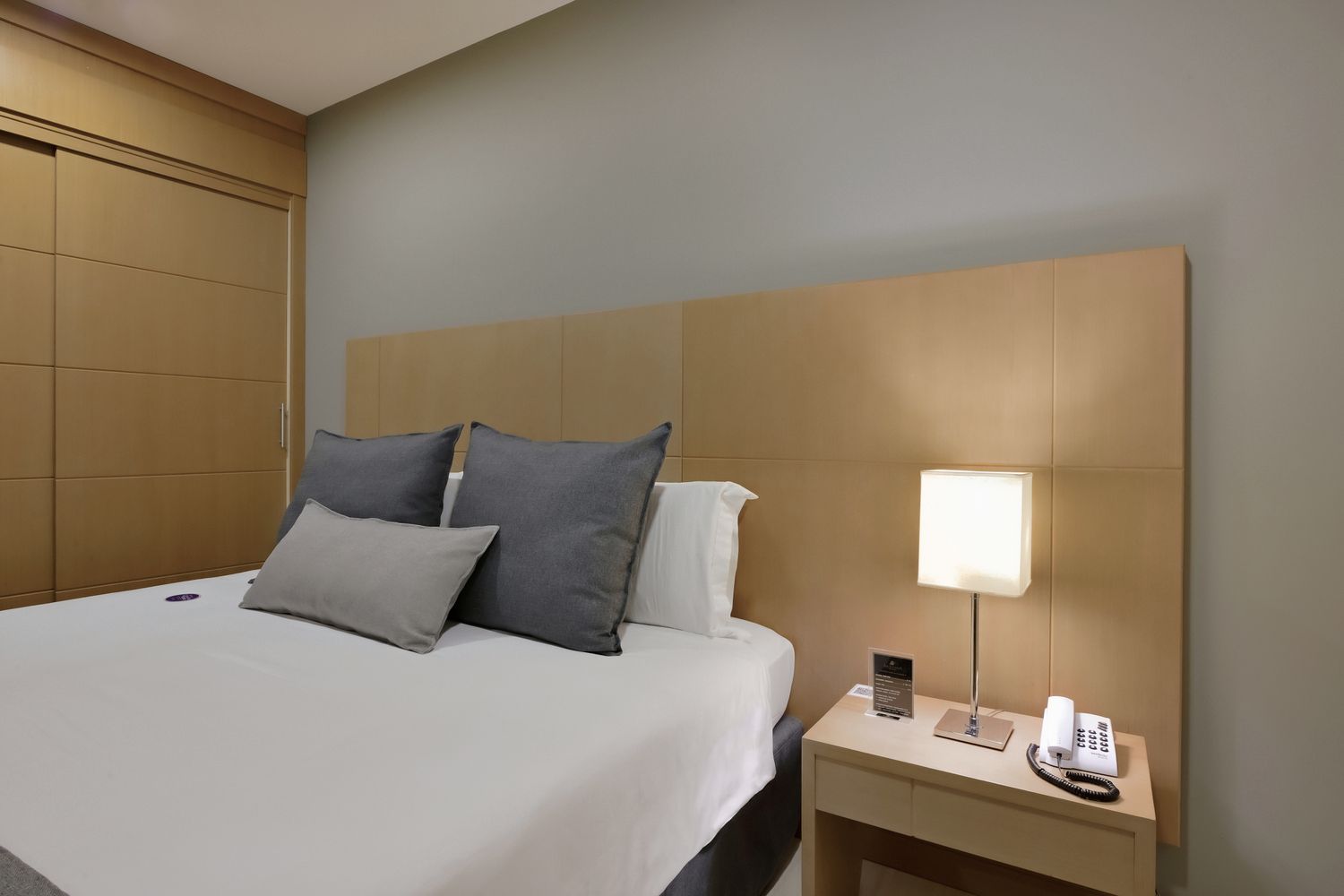 Um quarto de hotel com uma cama, mesa de cabeceira e abajur.