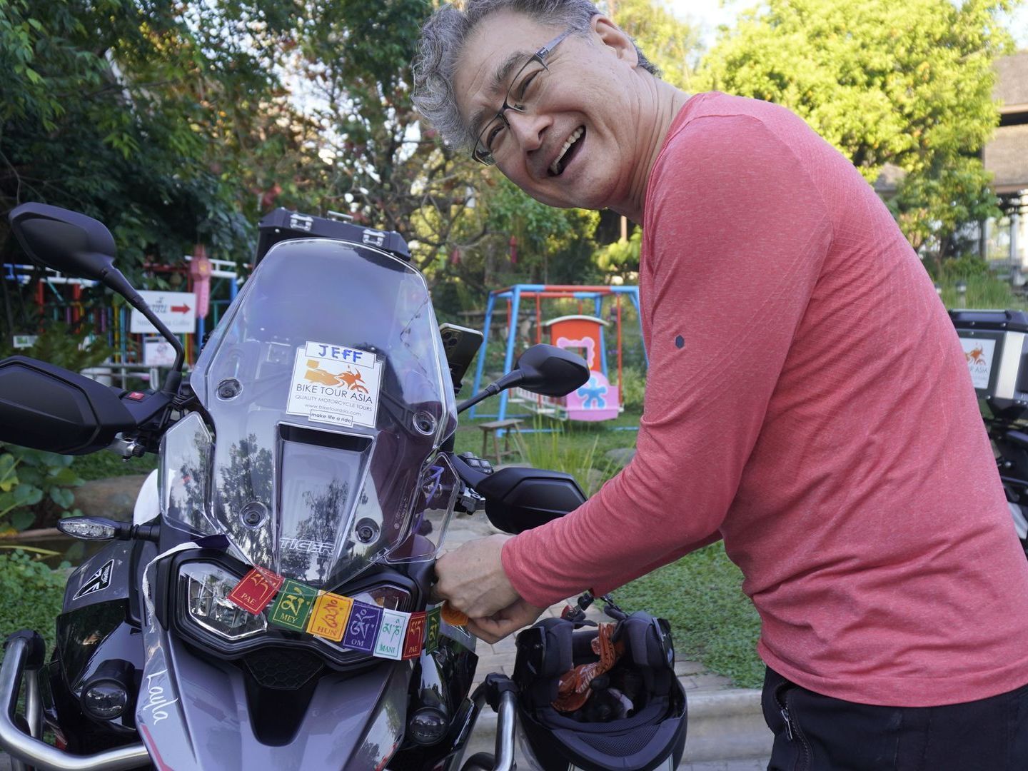 A man in a pink shirt is standing next to a motorcycle.
