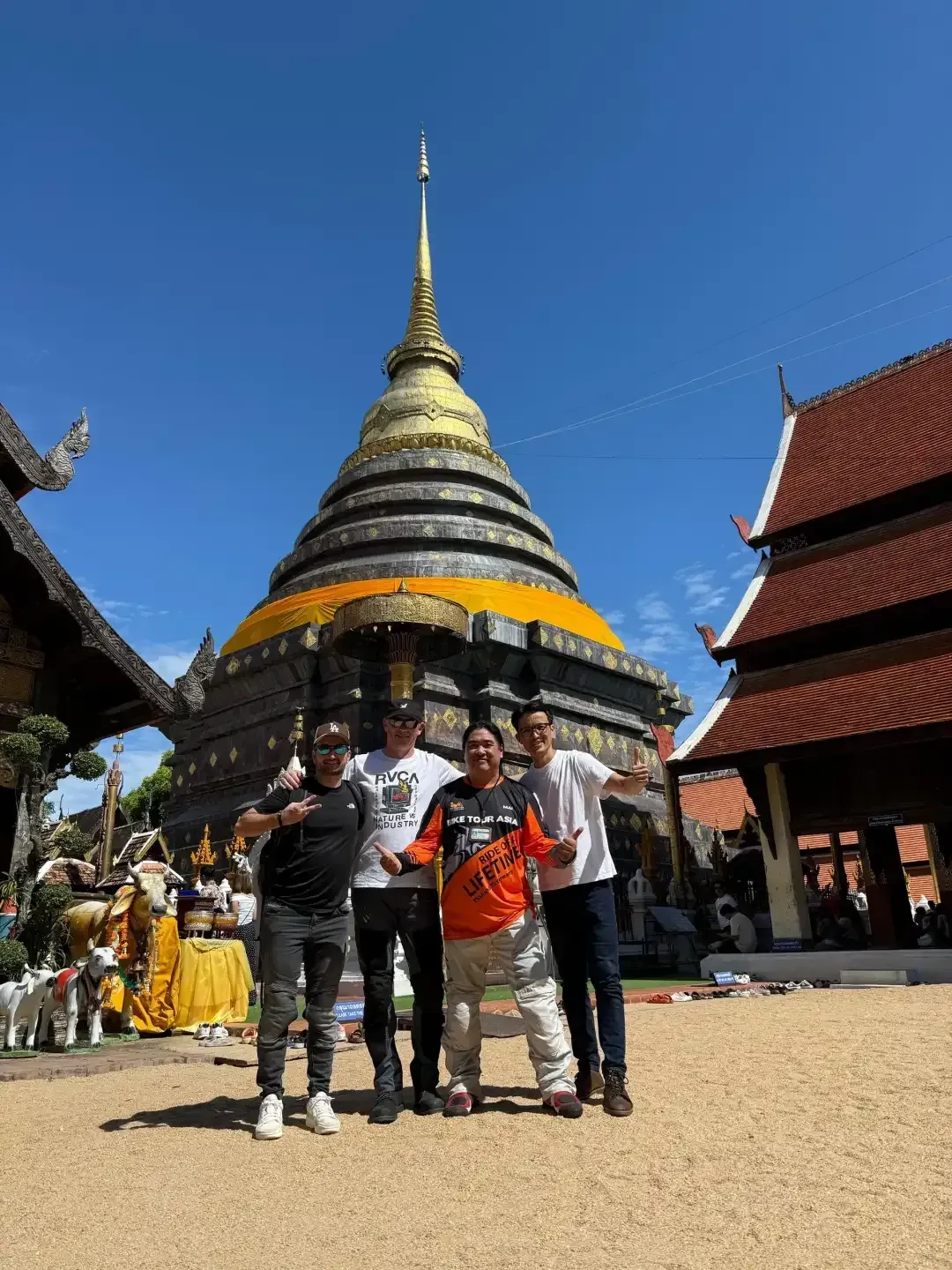 Bike Tour Asia riders visiting Wat Phra That Lampang Luang temple with golden stupa under blue sky in northern Thailand
